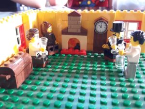 Lego room with four Lego minifigure men holding glasses sitting around a fireplace