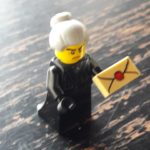 Lego minifigure old woman holding package, with grey hair in a bun, angry expression and black dress