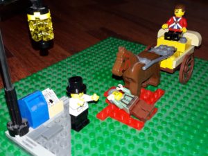 Lego minifigure lying on red tiles representing blood, under a Lego horse pulling a carriage, with Lego minifigure man watching