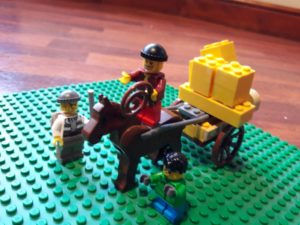 Lego horse drawing a cart overloaded with Lego bricks, with Lego minifigures brandishing a whip and a stick