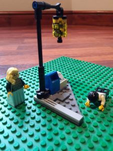 Lego minifigure man lying face down near a Lego lamp post, watched by a Lego minifigure girl